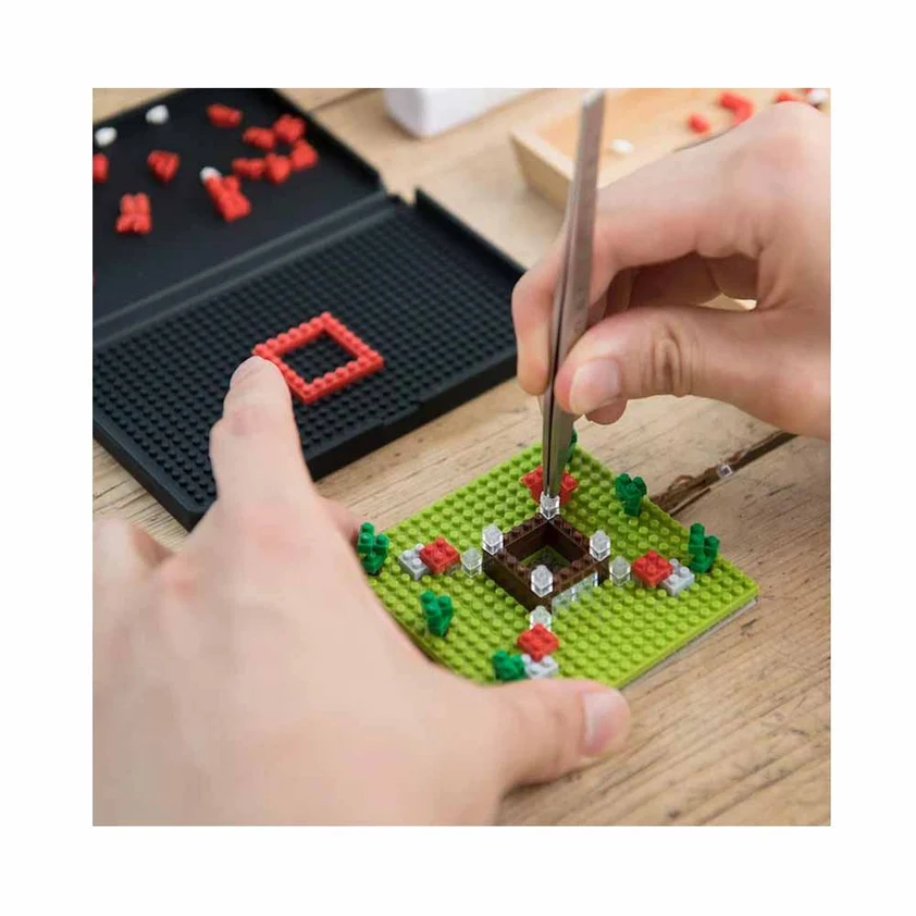 Hands using nanoblock tweezers to place a brick on a green baseplate resting on a building pad