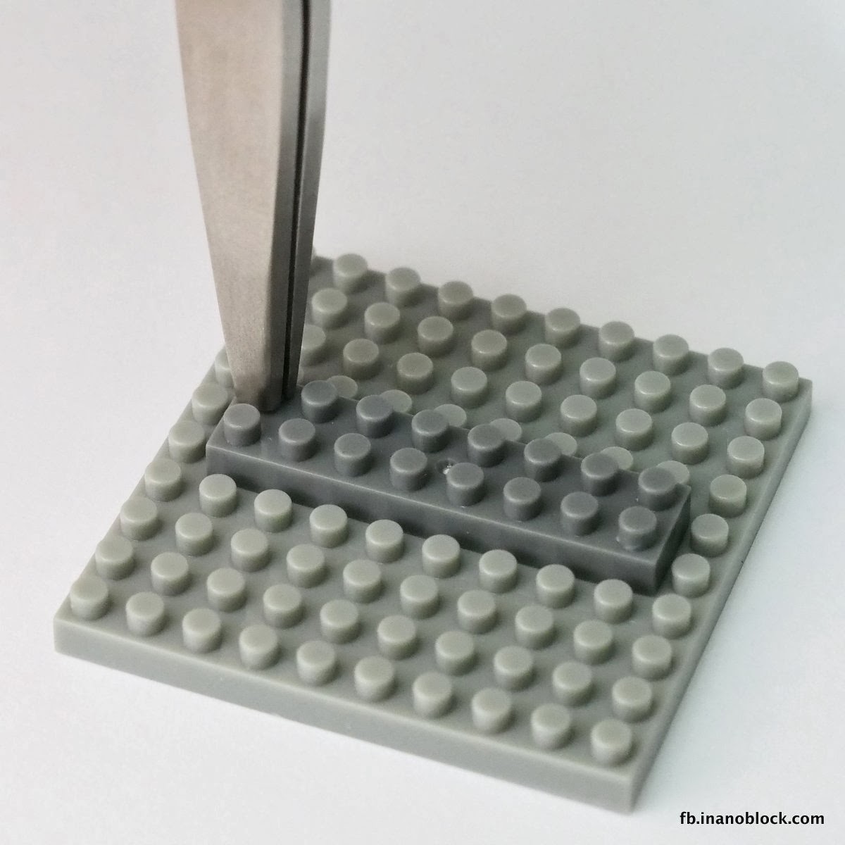 Tweezers gripping a single stud on a gray nanoblock plate and lifting straight up